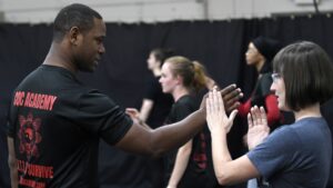 A black martial arts instructor teaches a blockig technique to a white female student