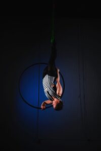 A woman in a black and white striped leotard and black tights performs an invert inside a black aerial hoop
